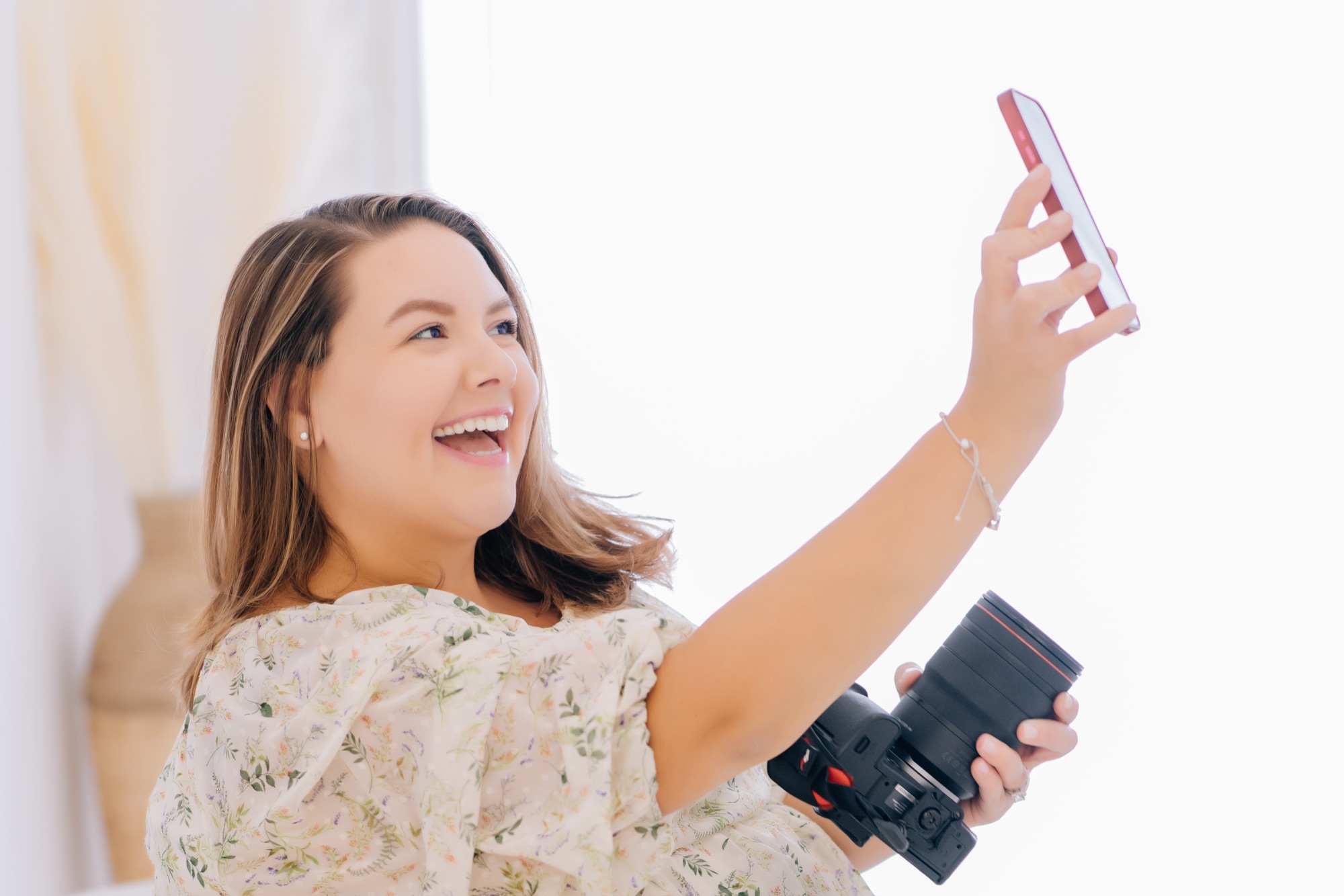 Content creator laughing while filming herself with a phone in one hand and a camera in the other