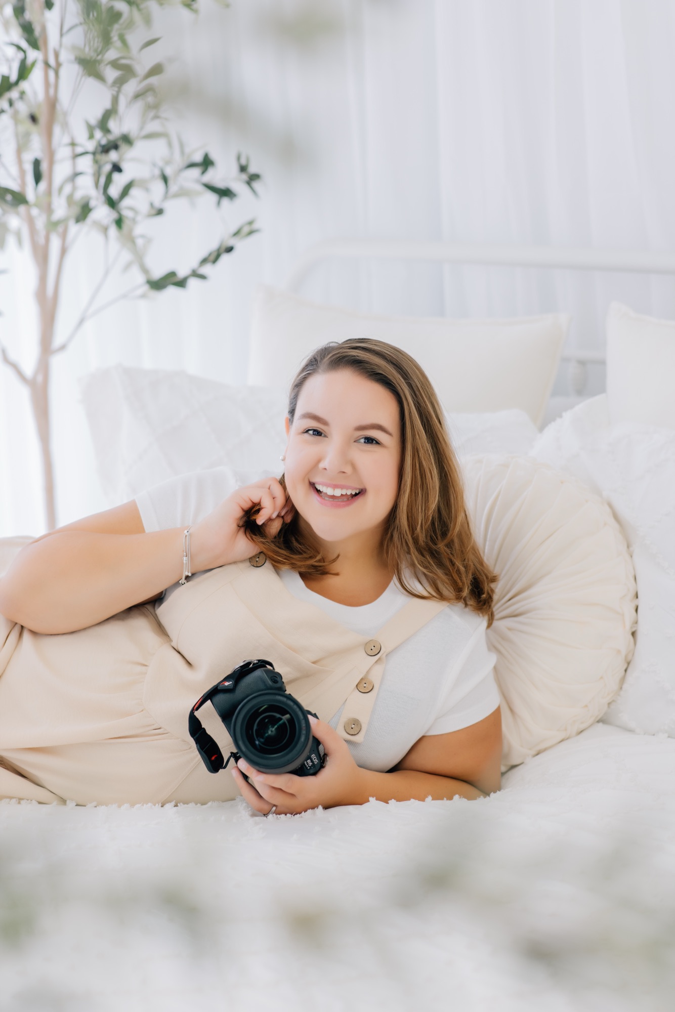 Marie relaxing on the studio's white bed setup with her camera in hand