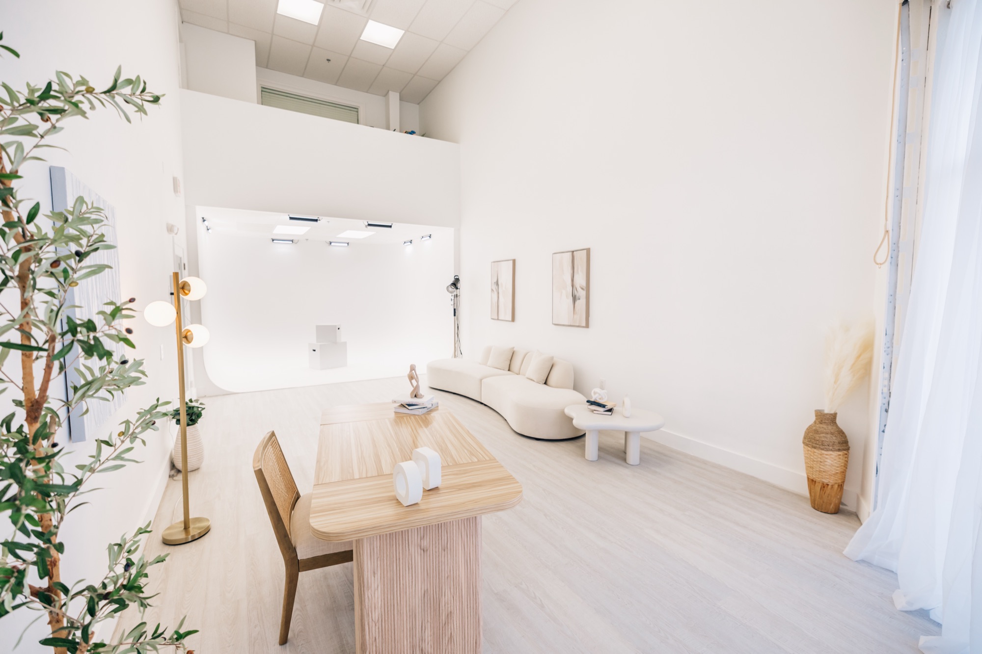 Wide view of the Four Little Birds studio — cyc wall, curved cream sofa, and branding desk in an all-white space