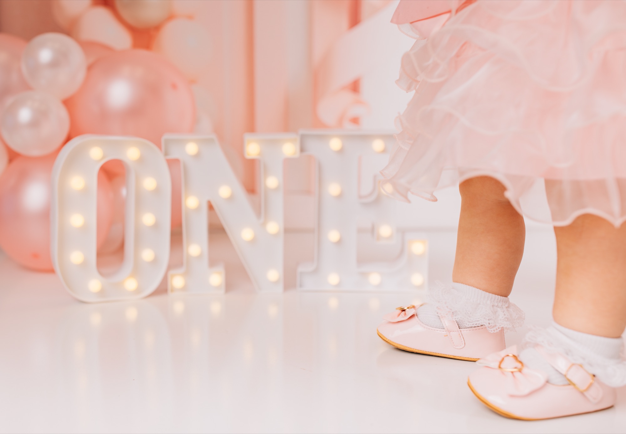 Toddler feet in frilly socks beside light-up ONE marquee letters