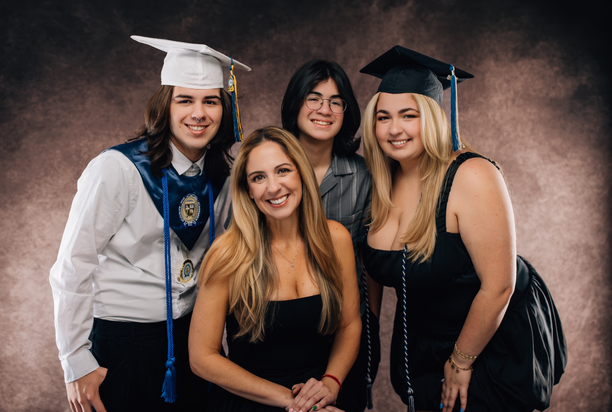 Mom with her three teens, two in caps and gowns with cords and medals, in the studio