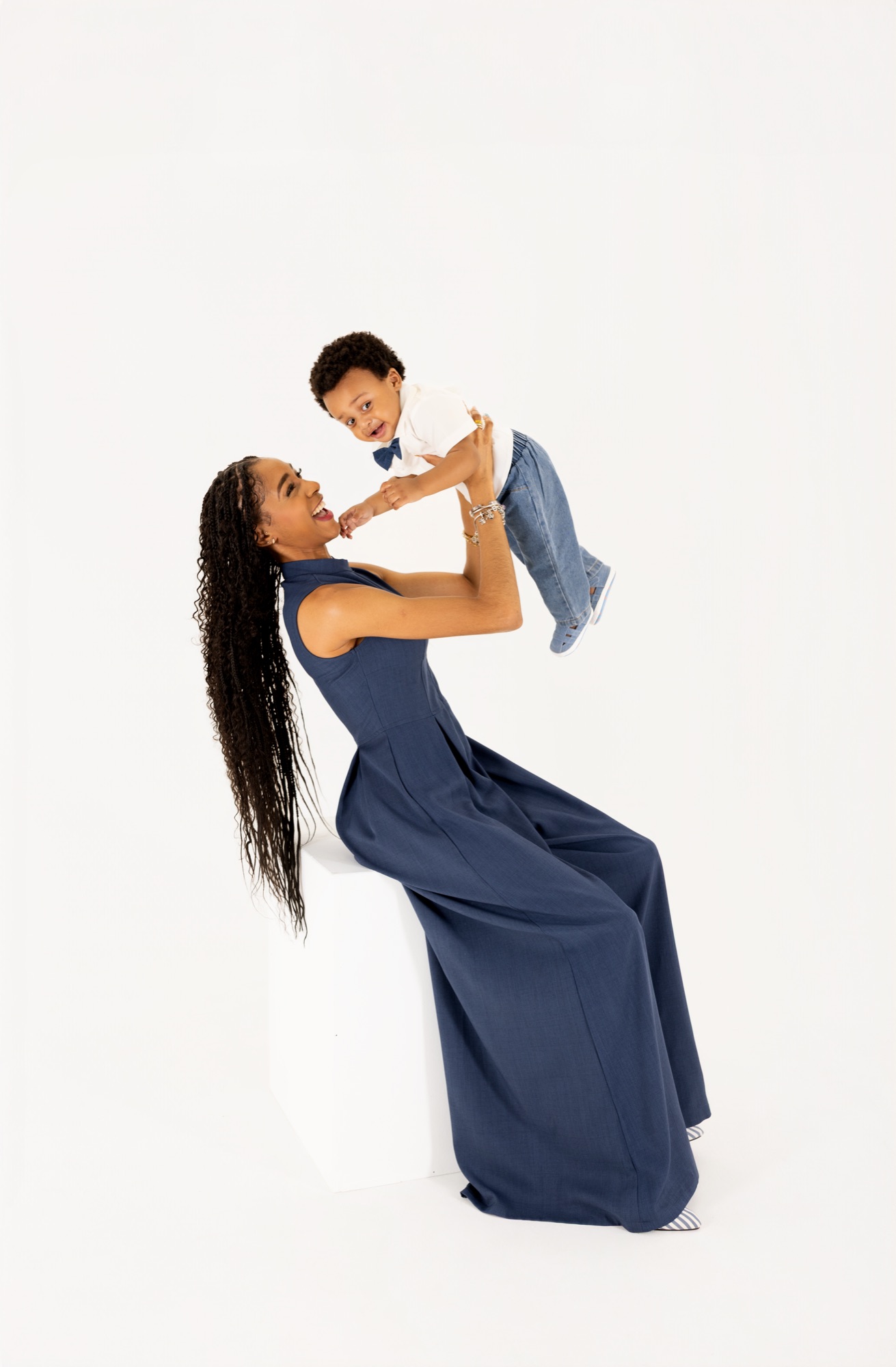 Mom in a navy dress lifting her baby boy overhead in a white studio