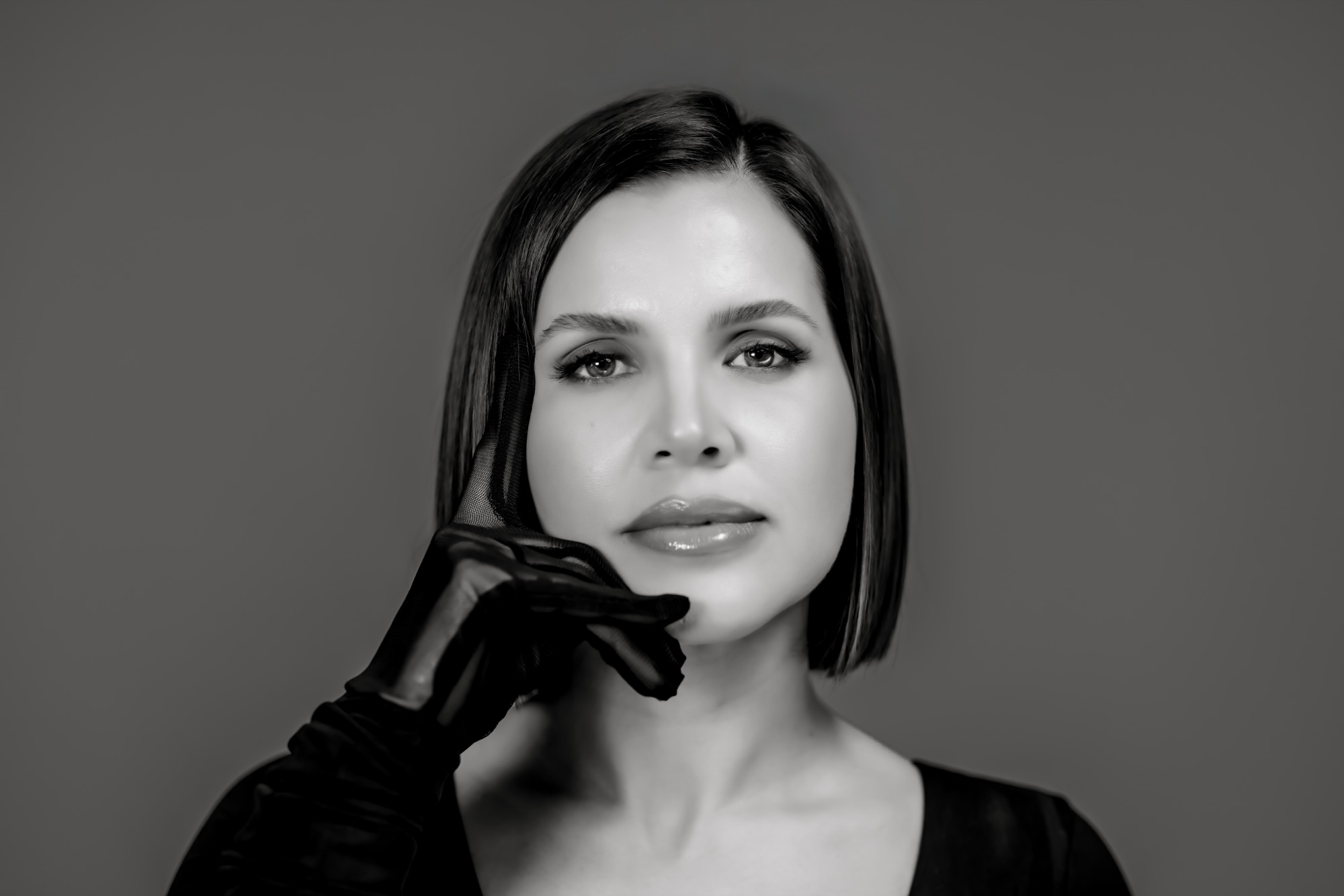 Black and white editorial portrait of a woman with a sheer glove at her chin