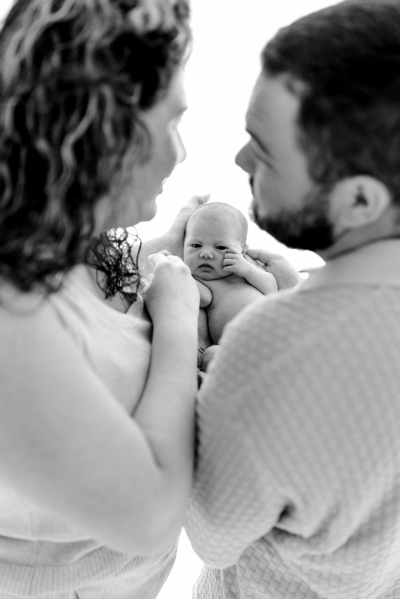Black and white over-the-shoulder image of parents cradling their awake newborn between them