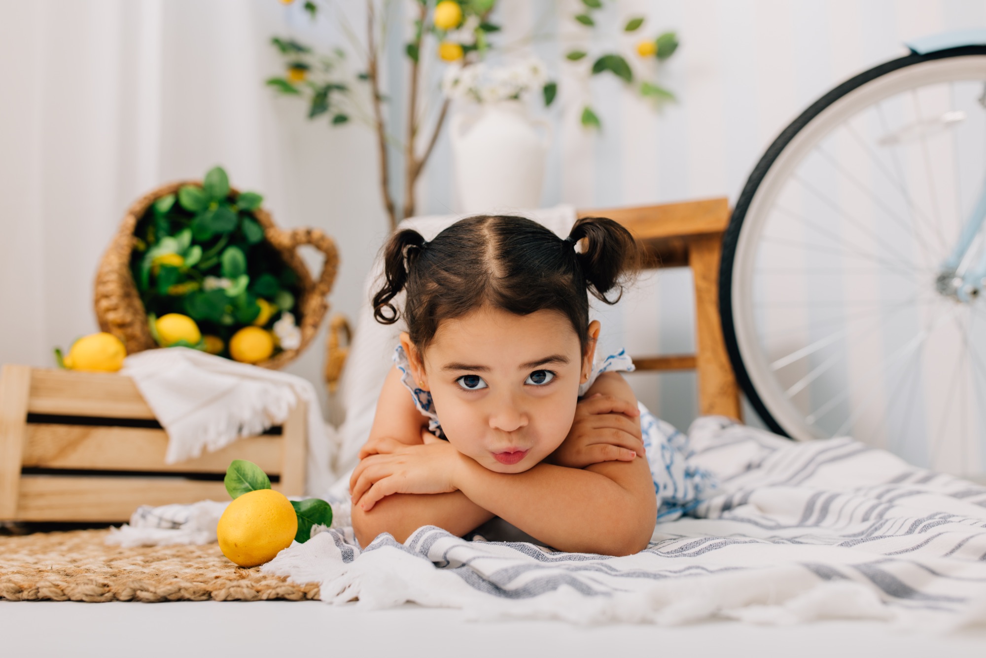 Toddler girl with pigtails lying chin on arms at a lemonade stand themed mini session