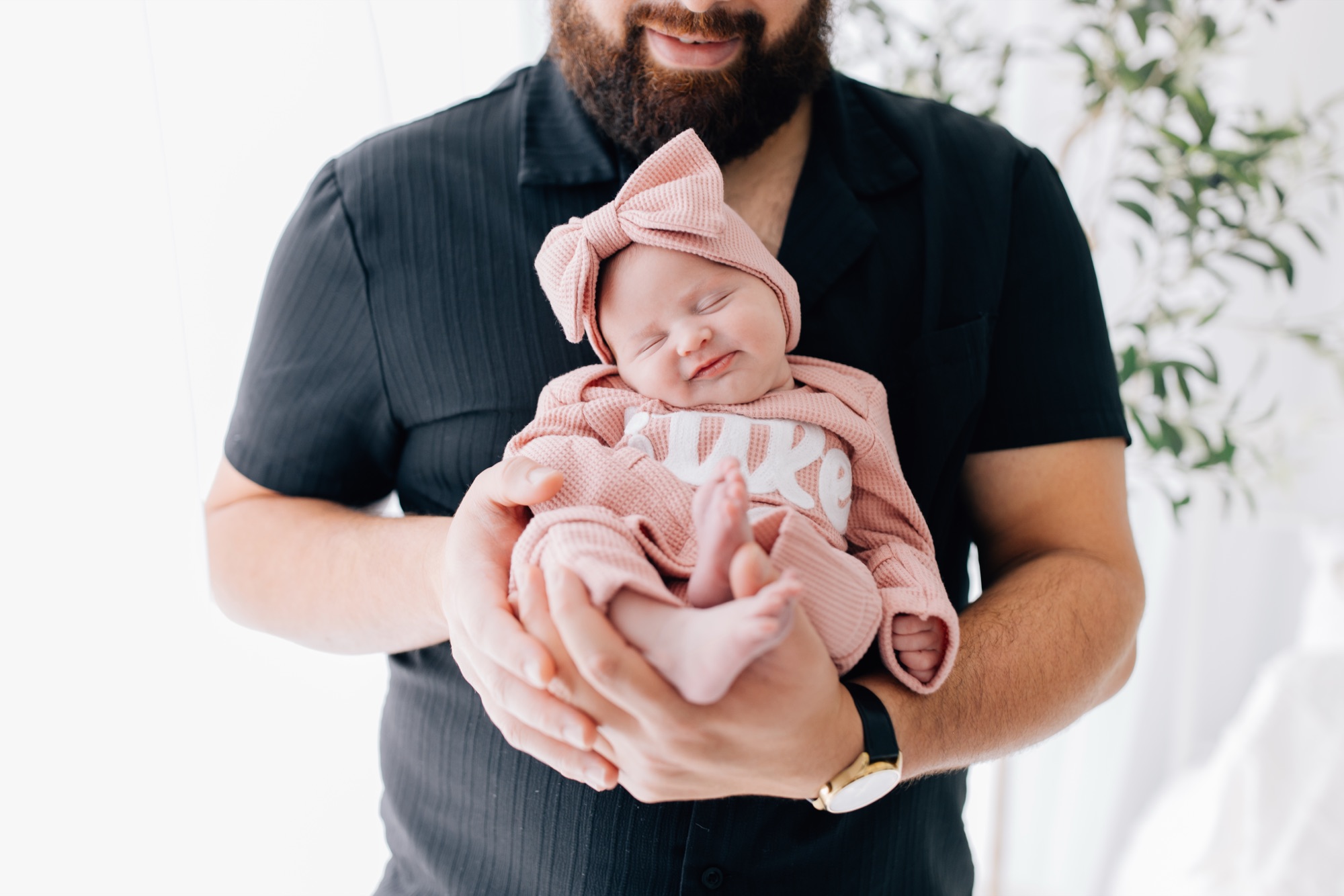 Dad cradling his sleeping newborn daughter in a pink knit outfit