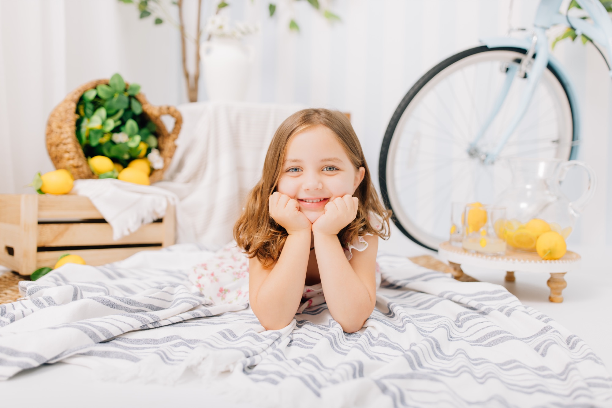 Girl lying on a striped blanket, chin in hands, at a lemonade stand mini session