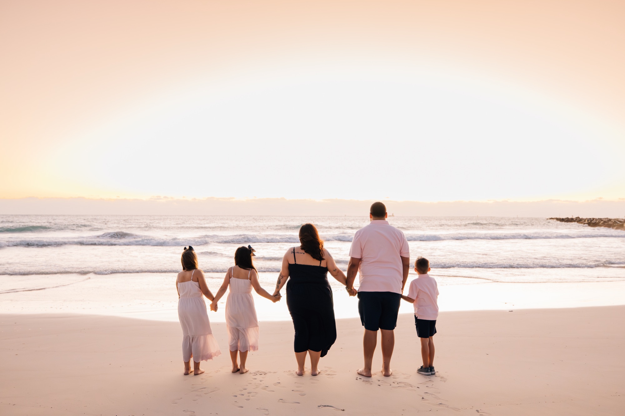 Family of five holding hands from behind on a beach at pastel sunset