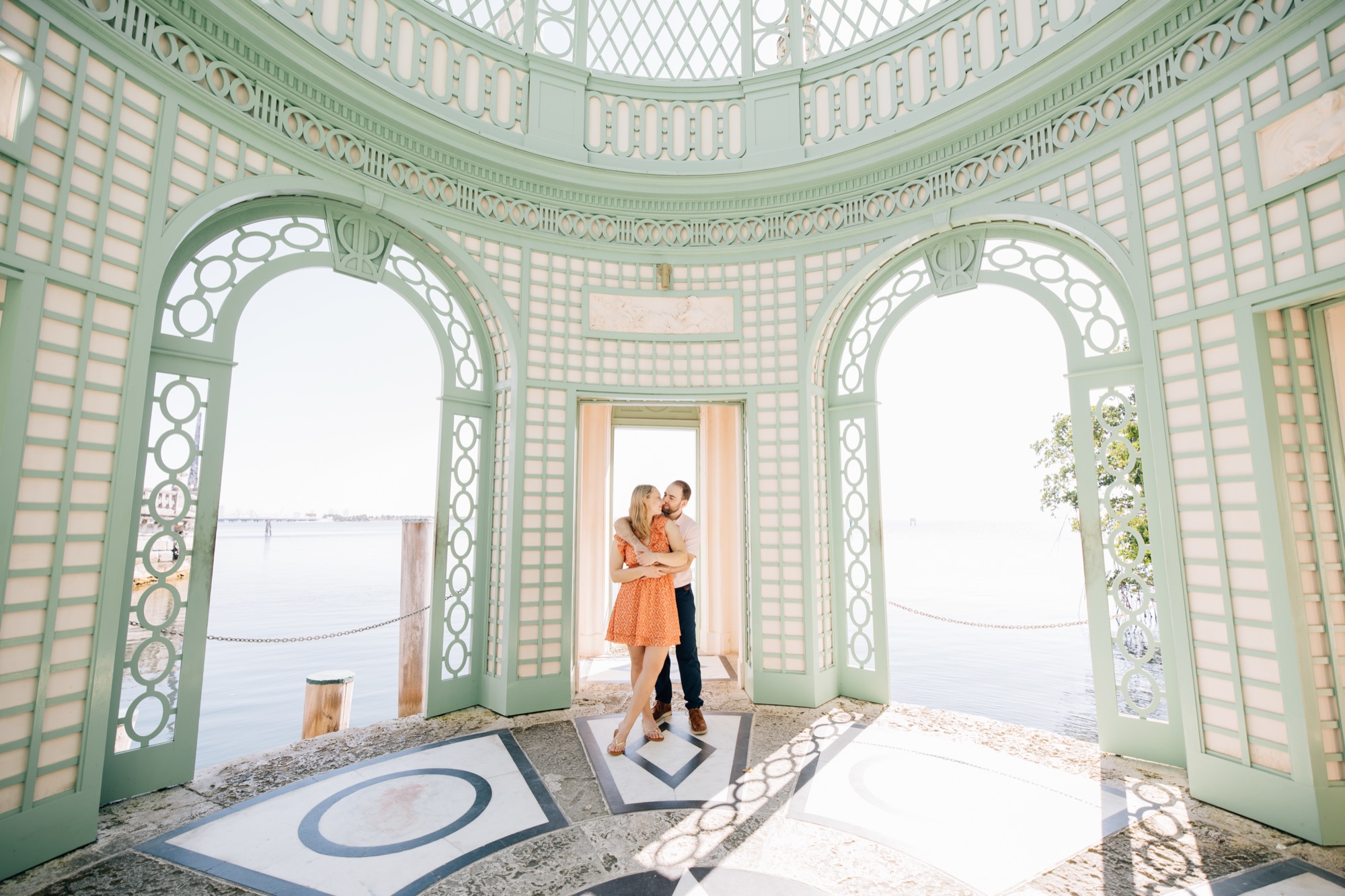Couple embracing in the doorway of the mint green lattice pavilion at Vizcaya over Biscayne Bay