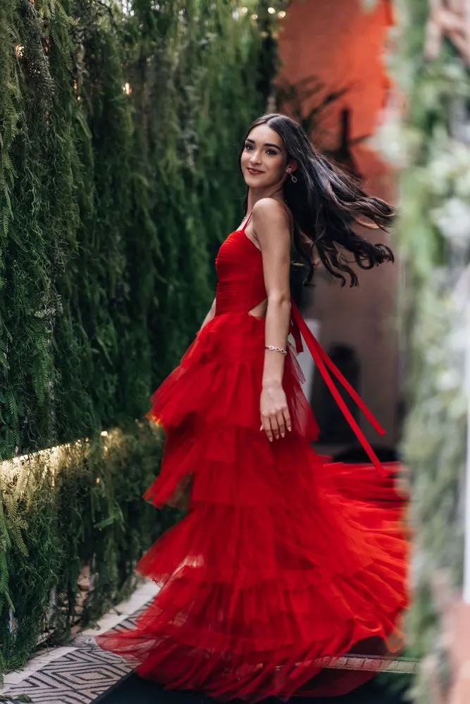 Woman twirling in a red tulle gown through a garden corridor