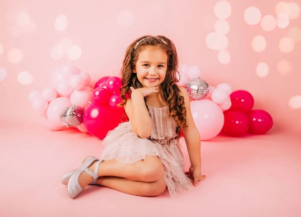 Birthday girl posing sweetly amid a pink balloon backdrop