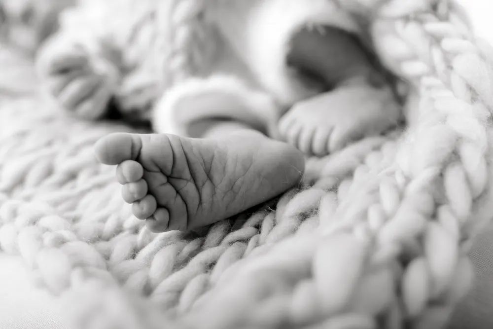 Black and white close-up of newborn feet and a tiny hand resting on a chunky knit blanket