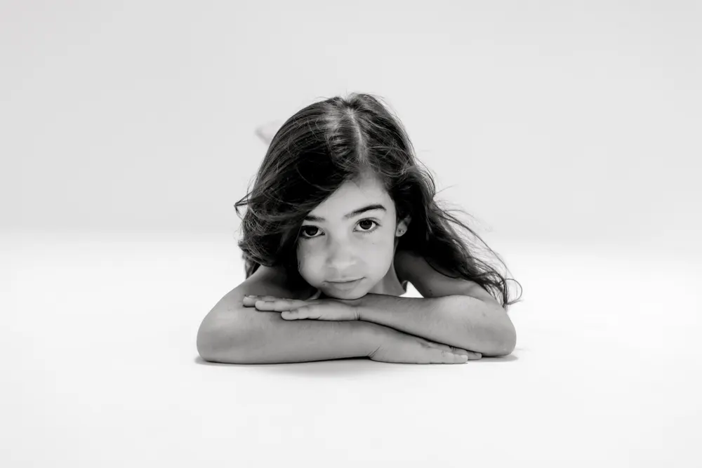 Black and white portrait of a girl lying on her stomach, chin on crossed arms, looking at the camera