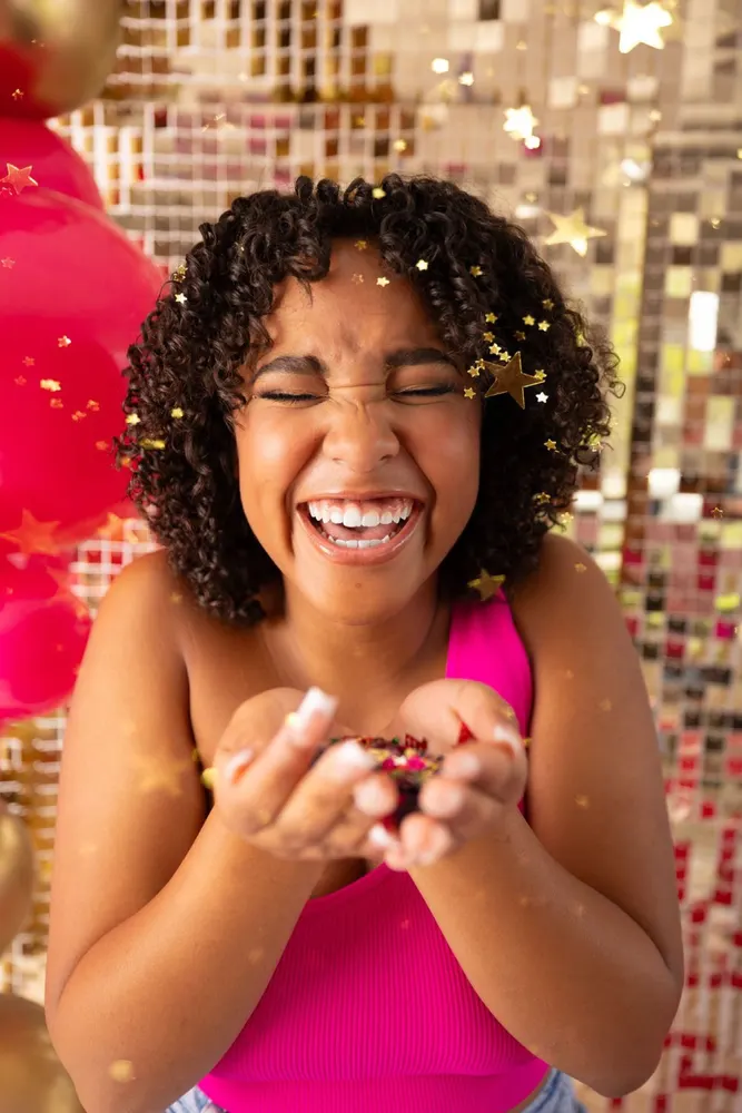 Teen laughing joyfully as gold confetti falls around her