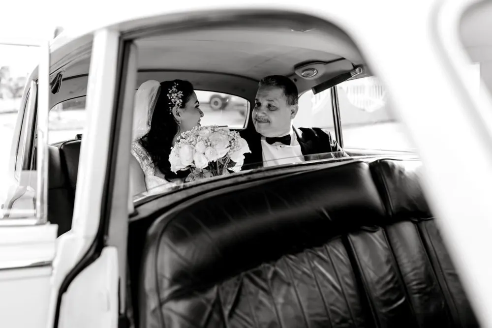 Bride and groom sharing a quiet look in the getaway car, captured in black and white