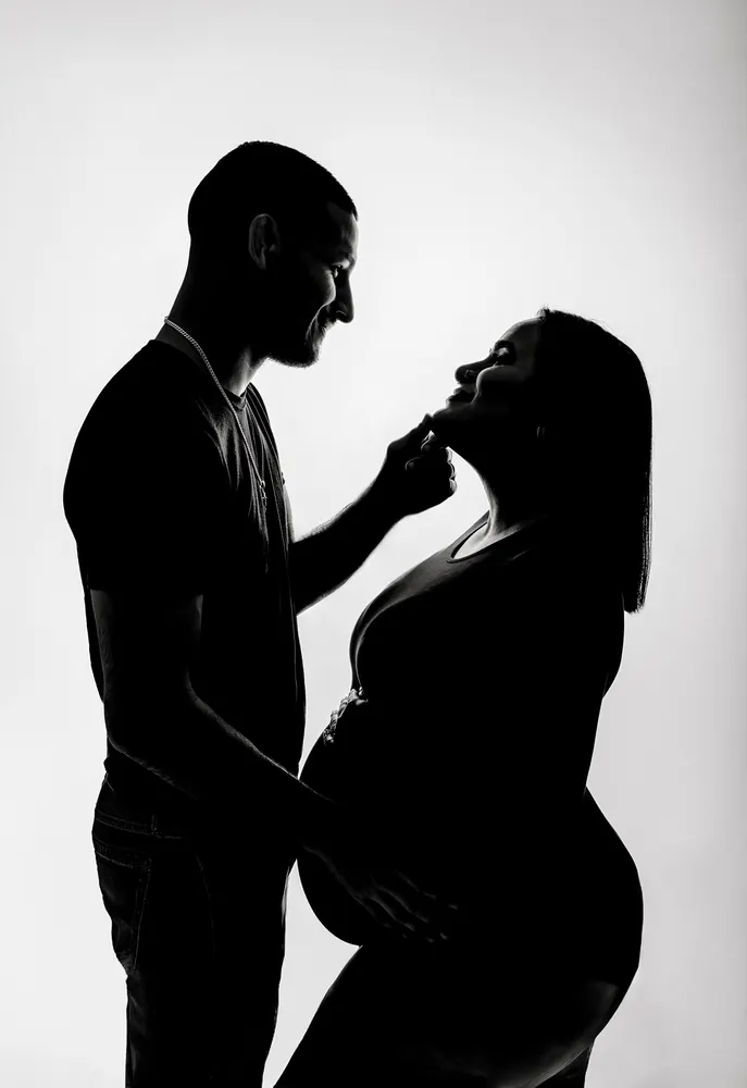 Backlit black and white silhouette of an expecting couple facing each other