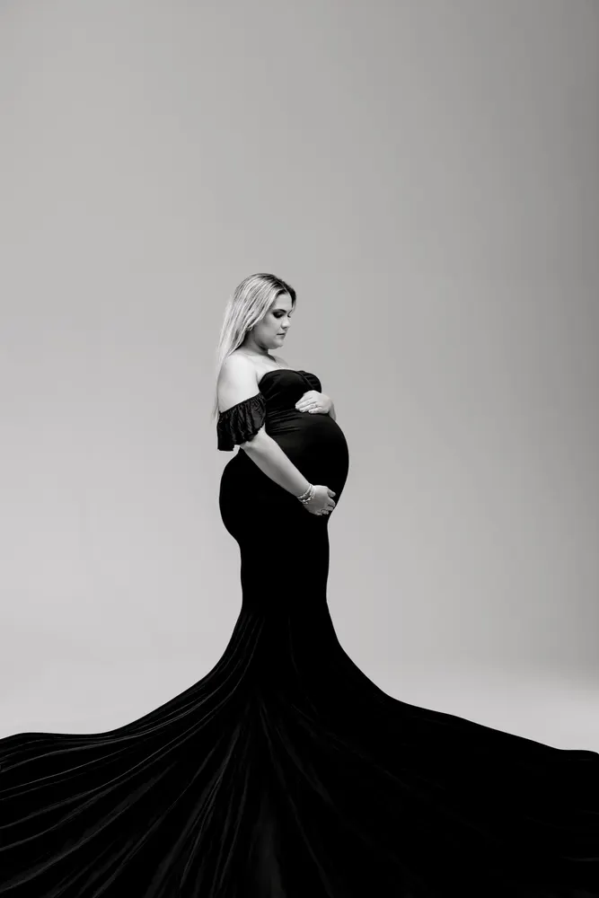 Black and white fine art maternity portrait in an off-shoulder gown with a fanned train