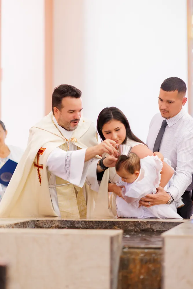 Priest pouring water over a baby held by the parents at a marble baptismal font