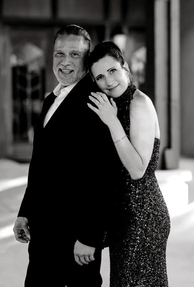 Black and white portrait of a couple in formal wear, her hands resting on his shoulder