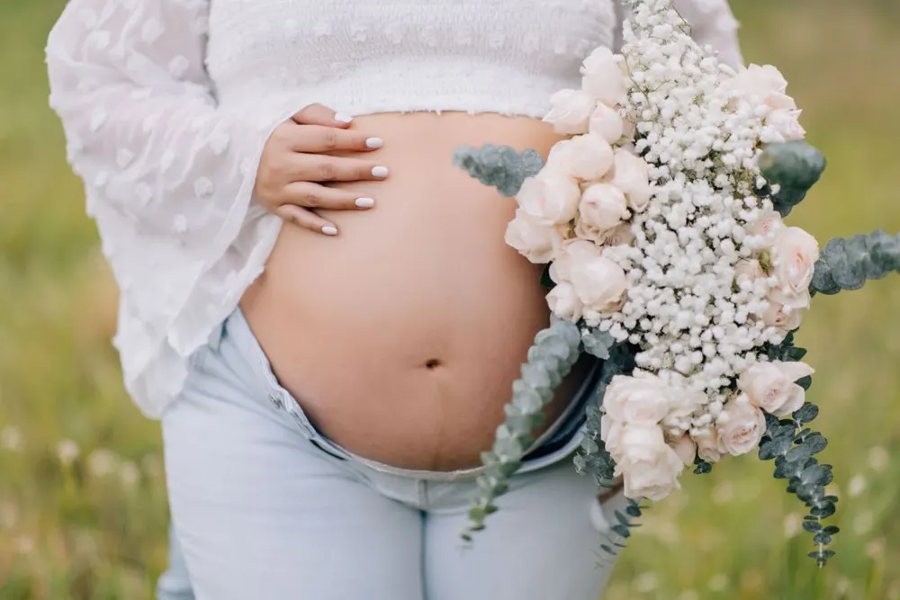 Close-up of a maternity bump cradled beside a blush rose bouquet