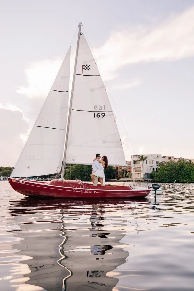 Couple embracing aboard a small red sailboat on calm Miami water at golden hour