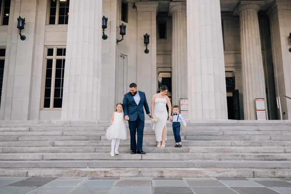 Newlywed couple descending courthouse steps hand in hand with their two young children