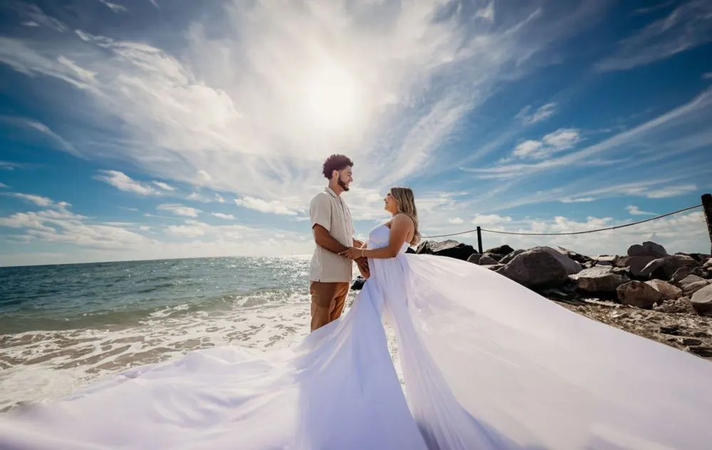 Bride's gown billowing in the ocean breeze as the couple embraces the sun