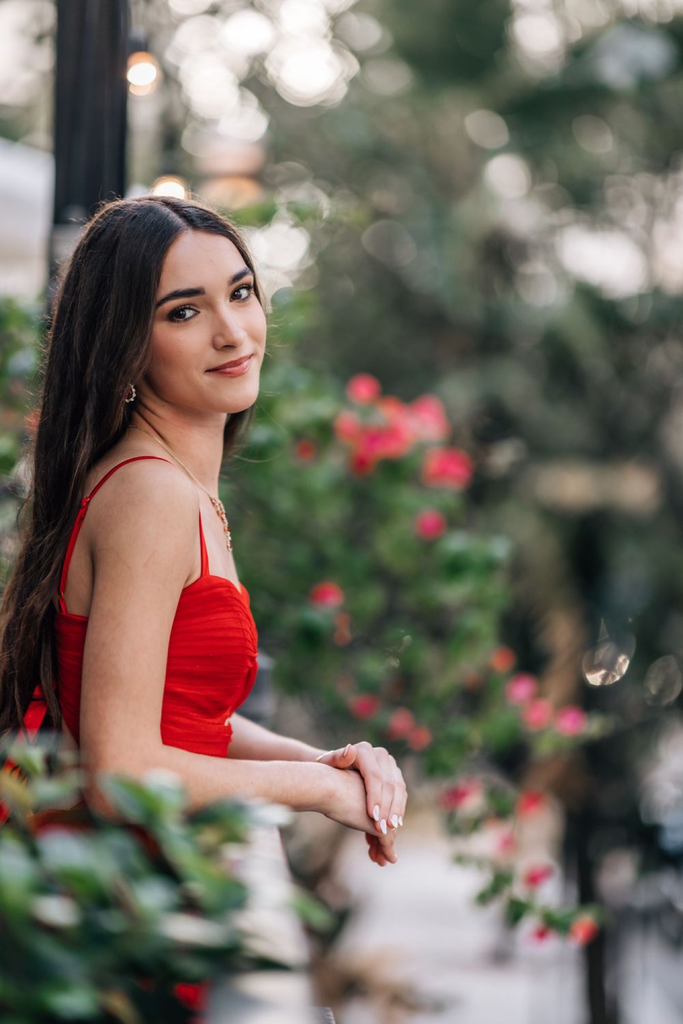 Portrait in a red dress leaning against a rose-covered railing