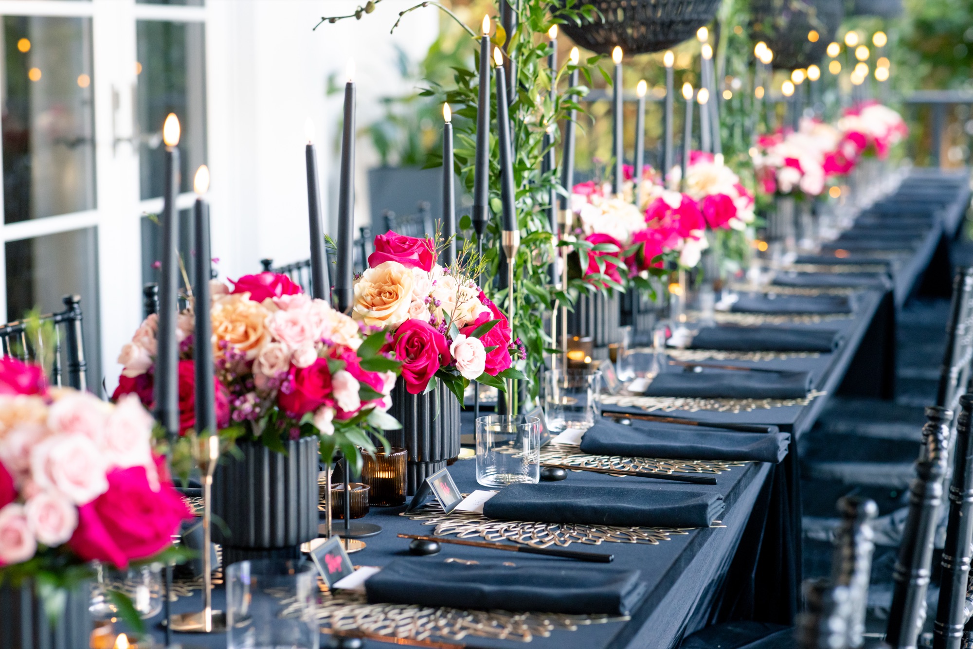 Event tablescape with black linens, gold placemats, taper candles and pink rose centerpieces