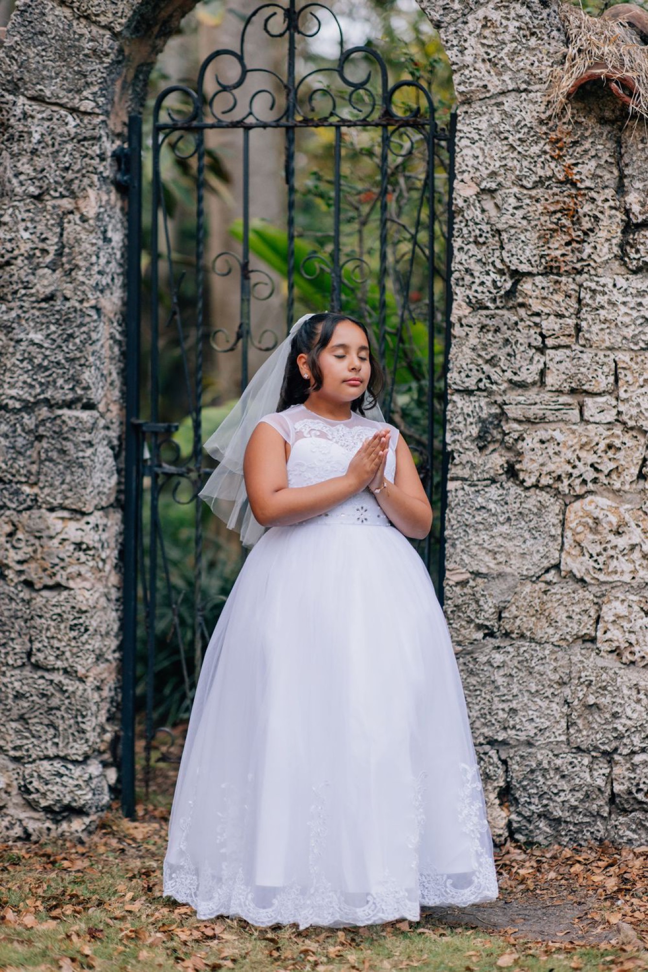 First communion portrait praying quietly at a garden's iron gate