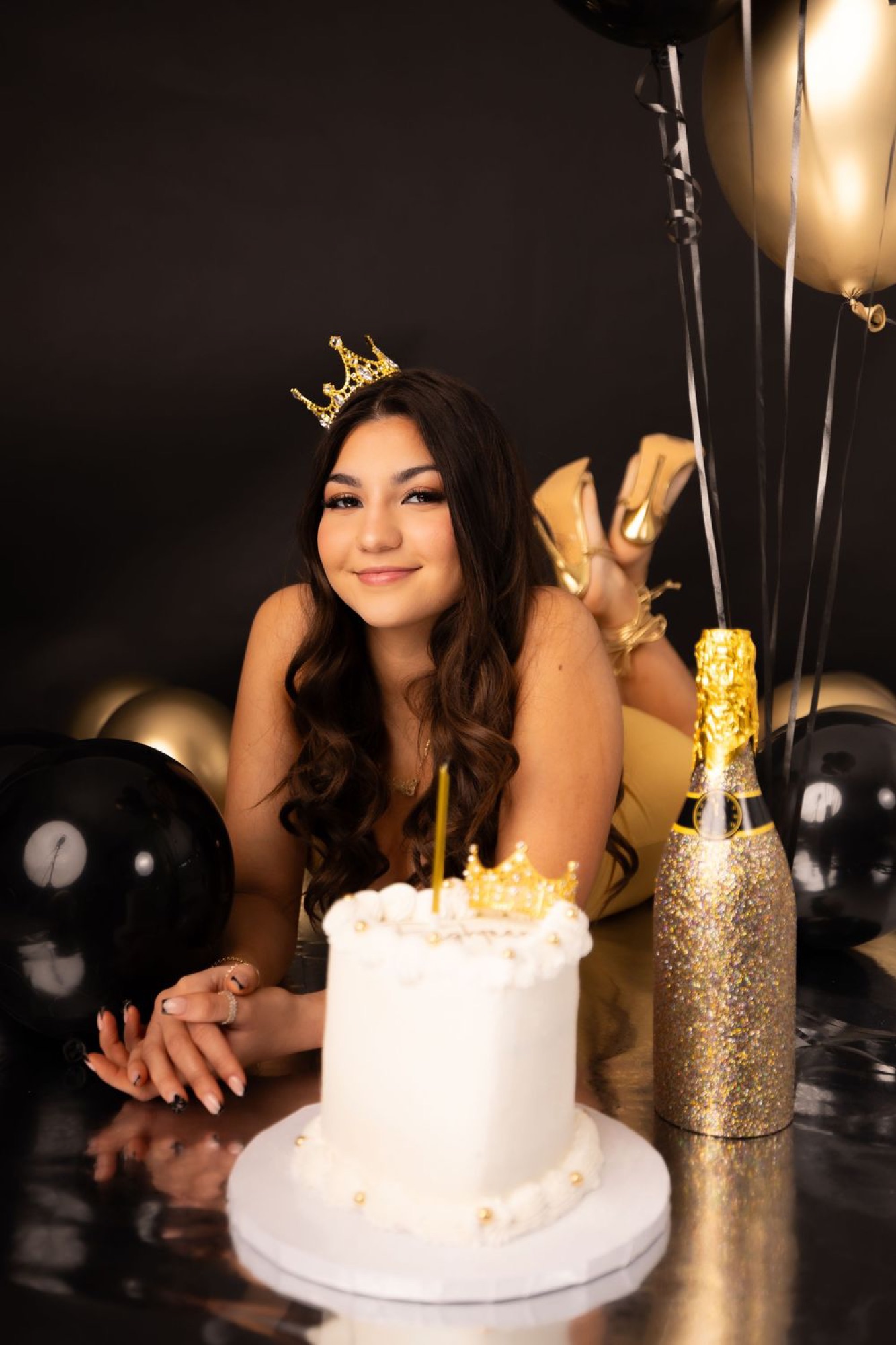 Quinceañera portrait with crown, cake, and gold celebration balloons