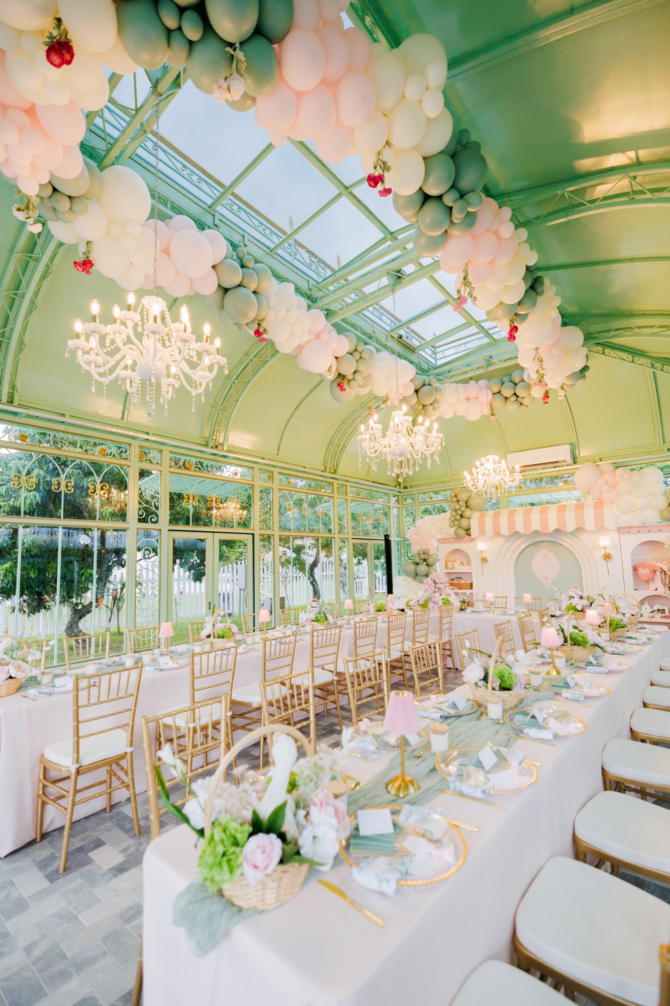 Glass conservatory venue dressed with balloon garlands, chandeliers and long blush tables