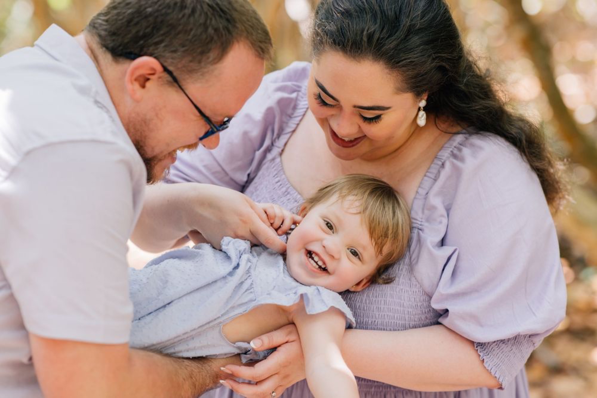 Parents playing with their laughing toddler in dappled forest light