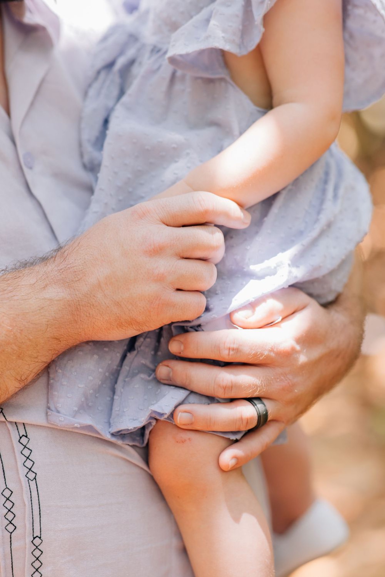 Detail shot of a father's hands gently holding his toddler close
