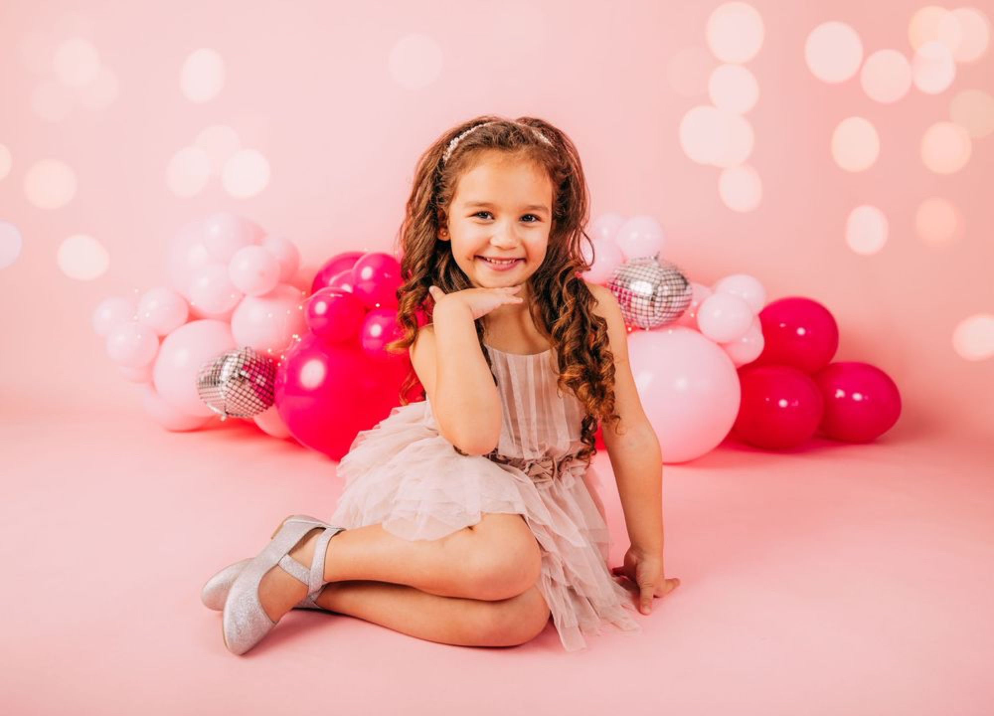 Birthday girl posing sweetly amid a pink balloon backdrop