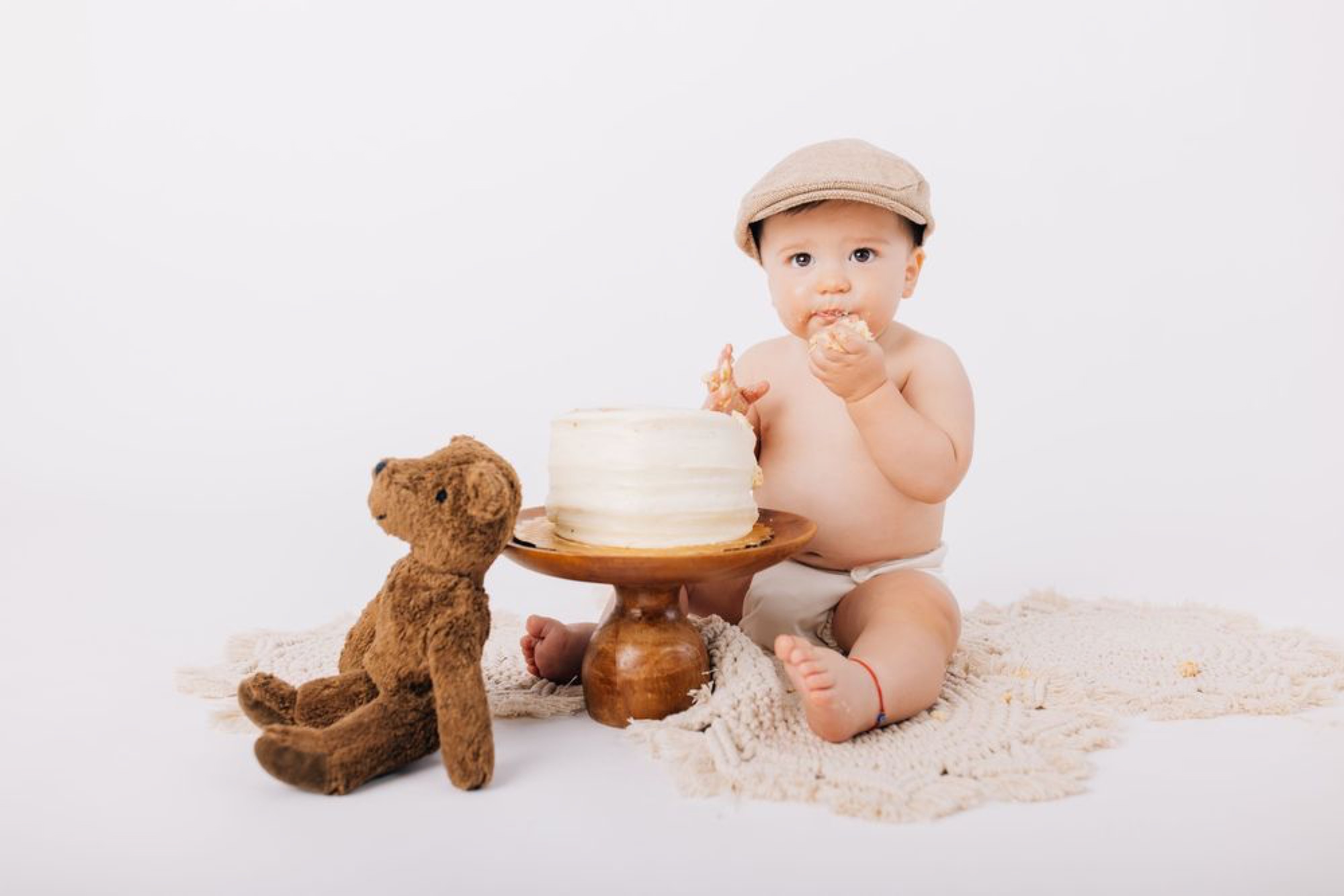 Baby boy digging into his cake smash beside a plush teddy bear