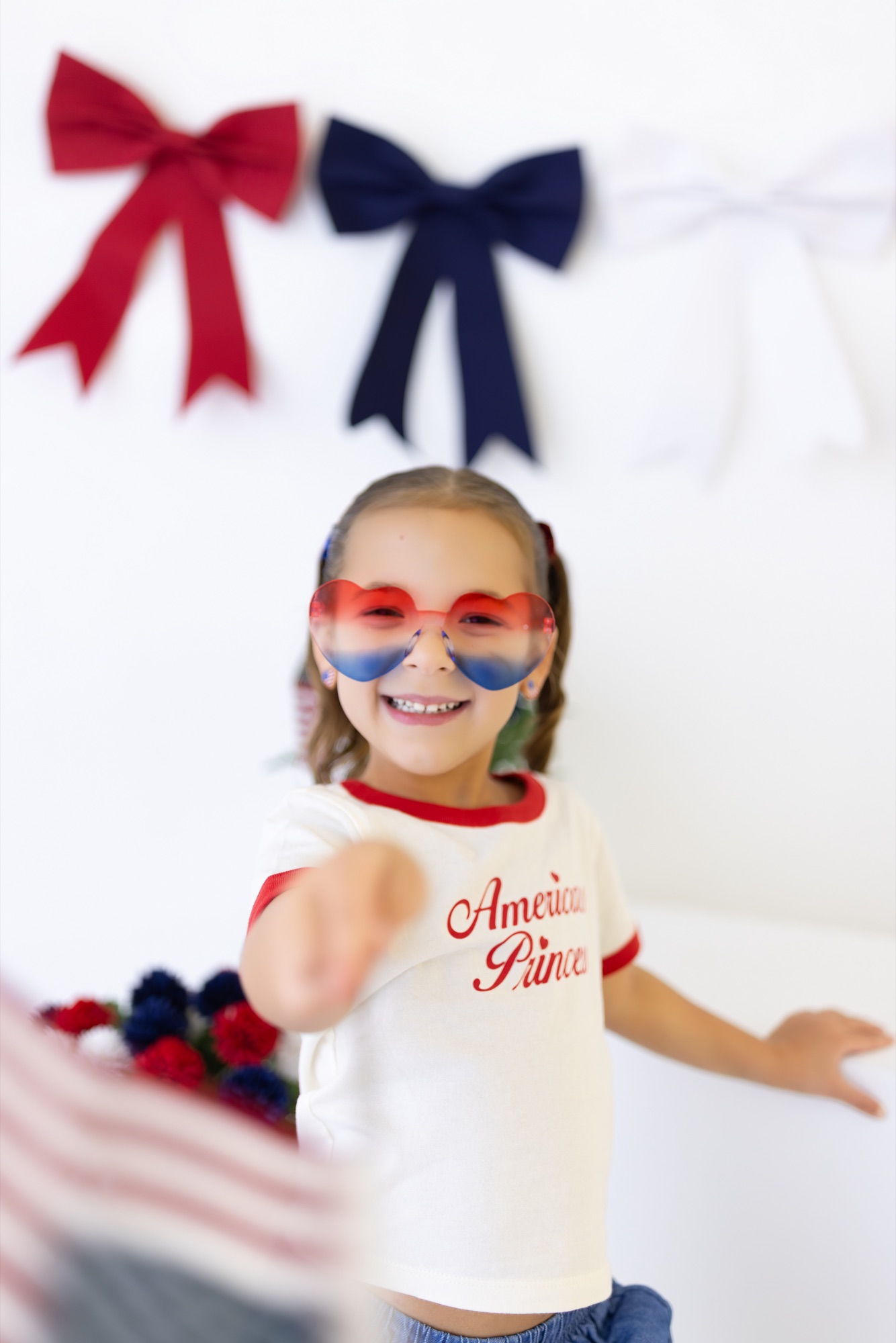 Girl in heart-shaped sunglasses reaching toward the camera at a Fourth of July mini session