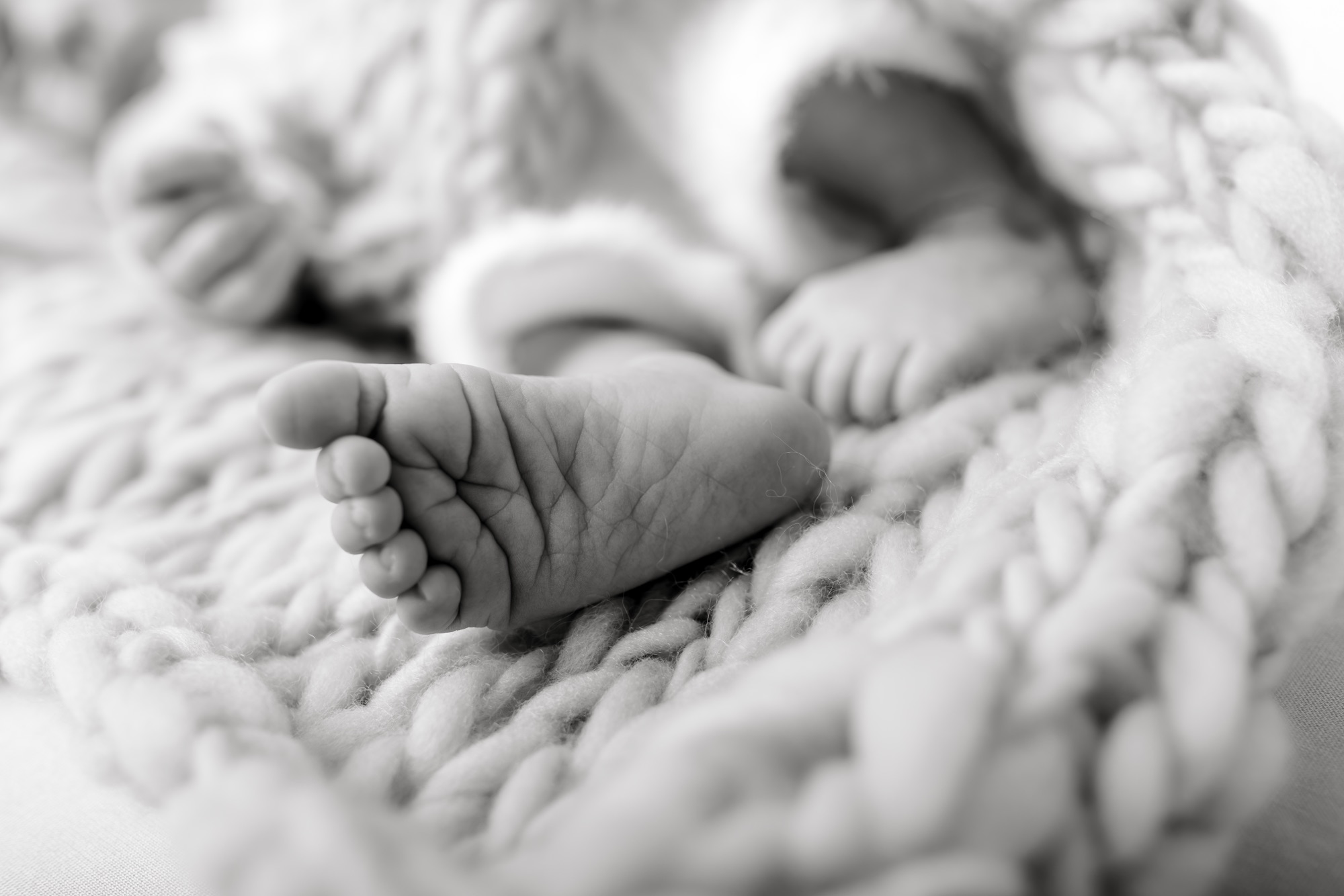 Black and white close-up of newborn feet and a tiny hand resting on a chunky knit blanket