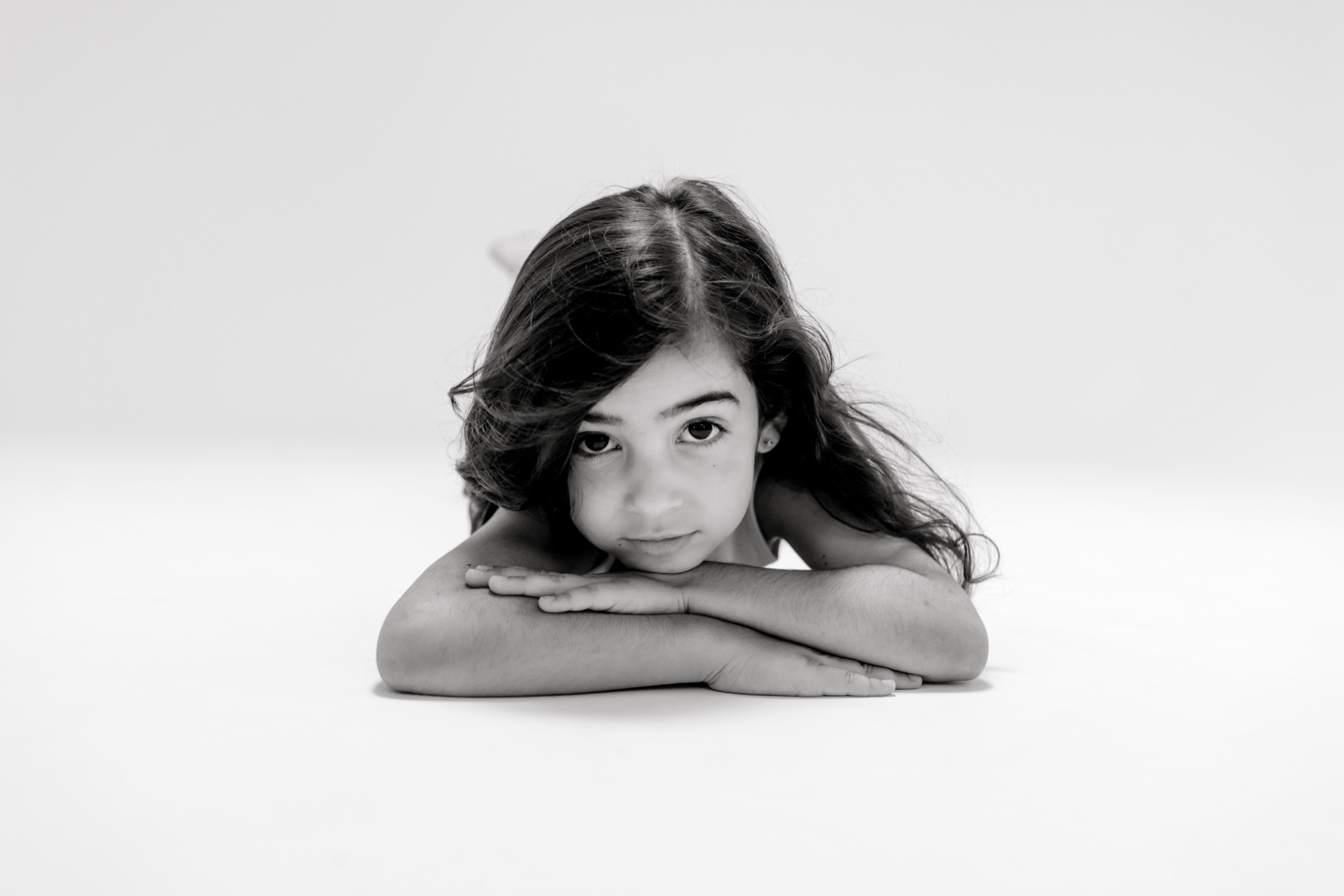 Black and white portrait of a girl lying on her stomach, chin on crossed arms, looking at the camera