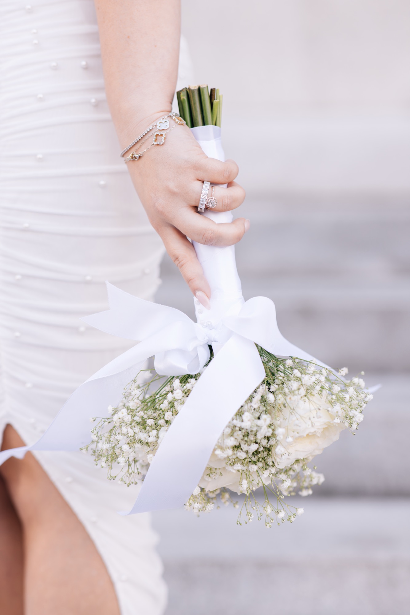 Bride's hands holding a baby's-breath bouquet wrapped in white ribbon against her pearl-studded dress