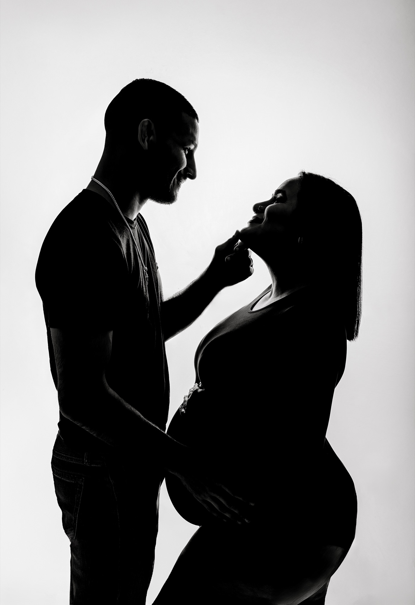 Backlit black and white silhouette of an expecting couple facing each other
