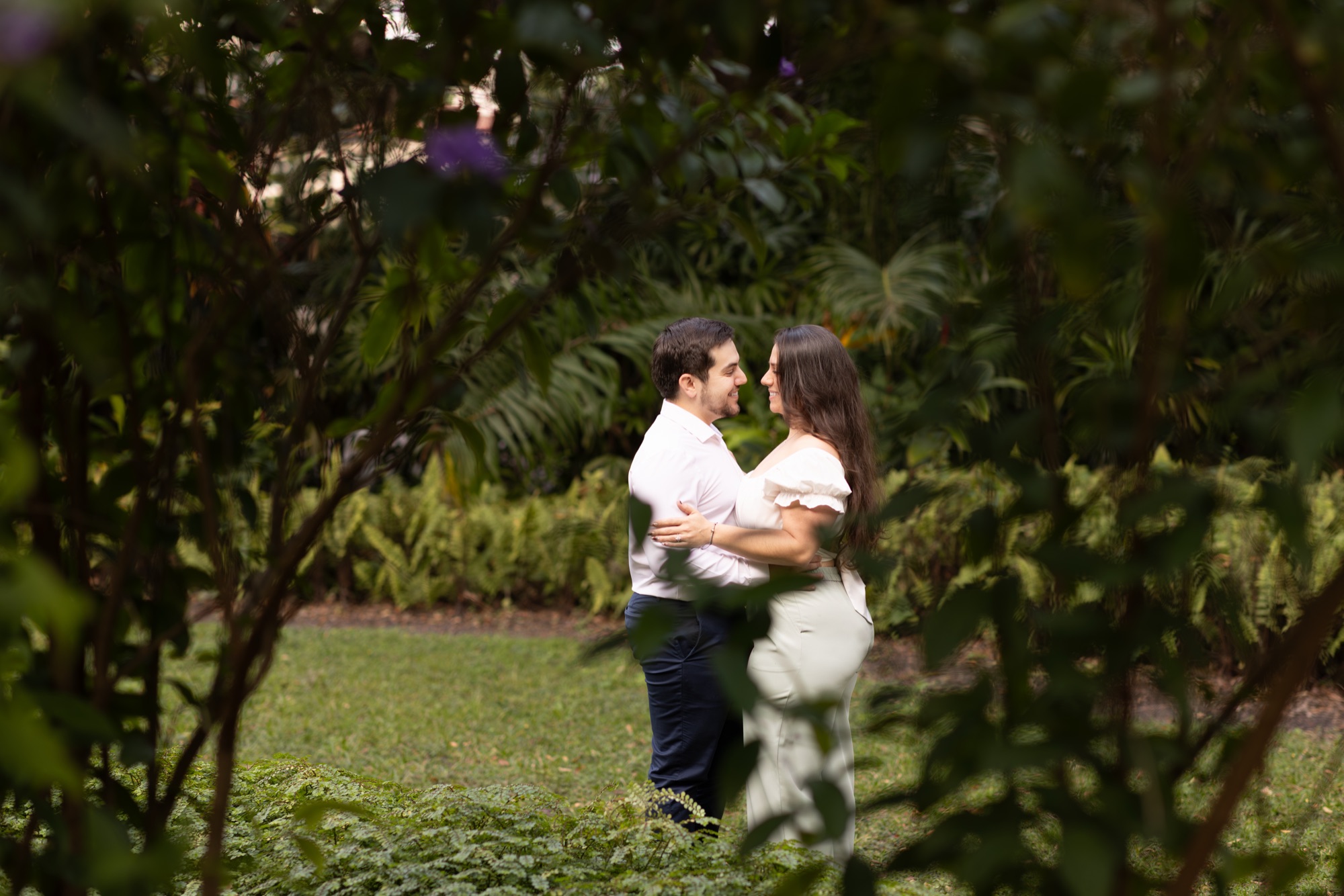 Couple embracing in a lush garden, framed through dark foliage