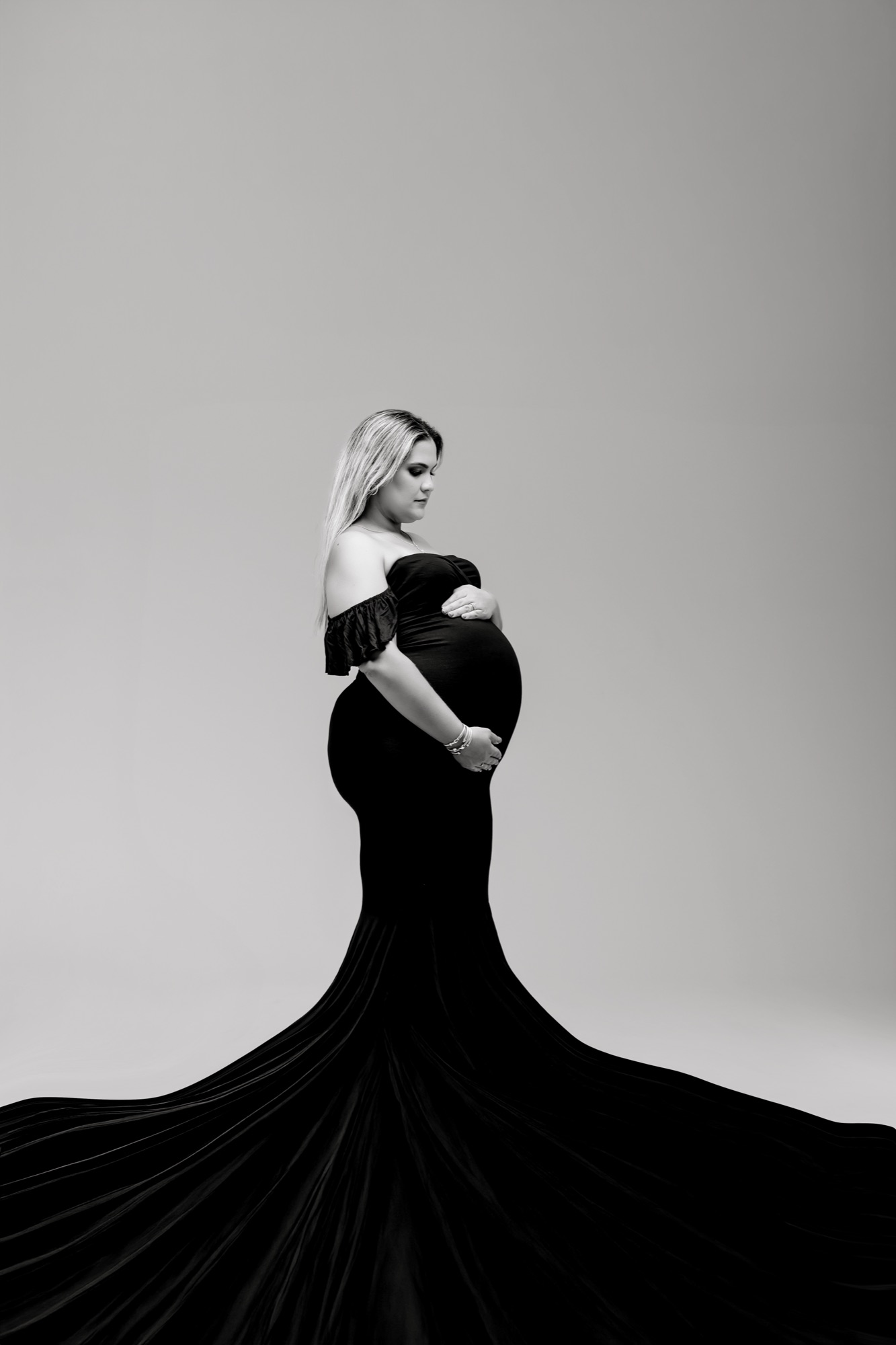 Black and white fine art maternity portrait in an off-shoulder gown with a fanned train