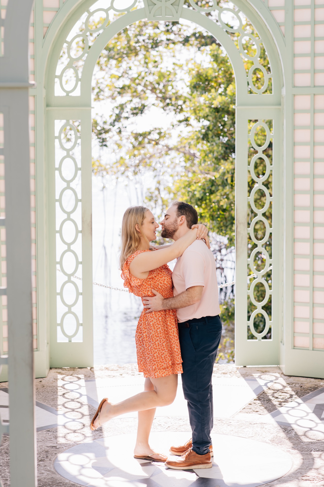 Couple kissing in the mint-green latticework gazebo at Vizcaya, water stretching behind them