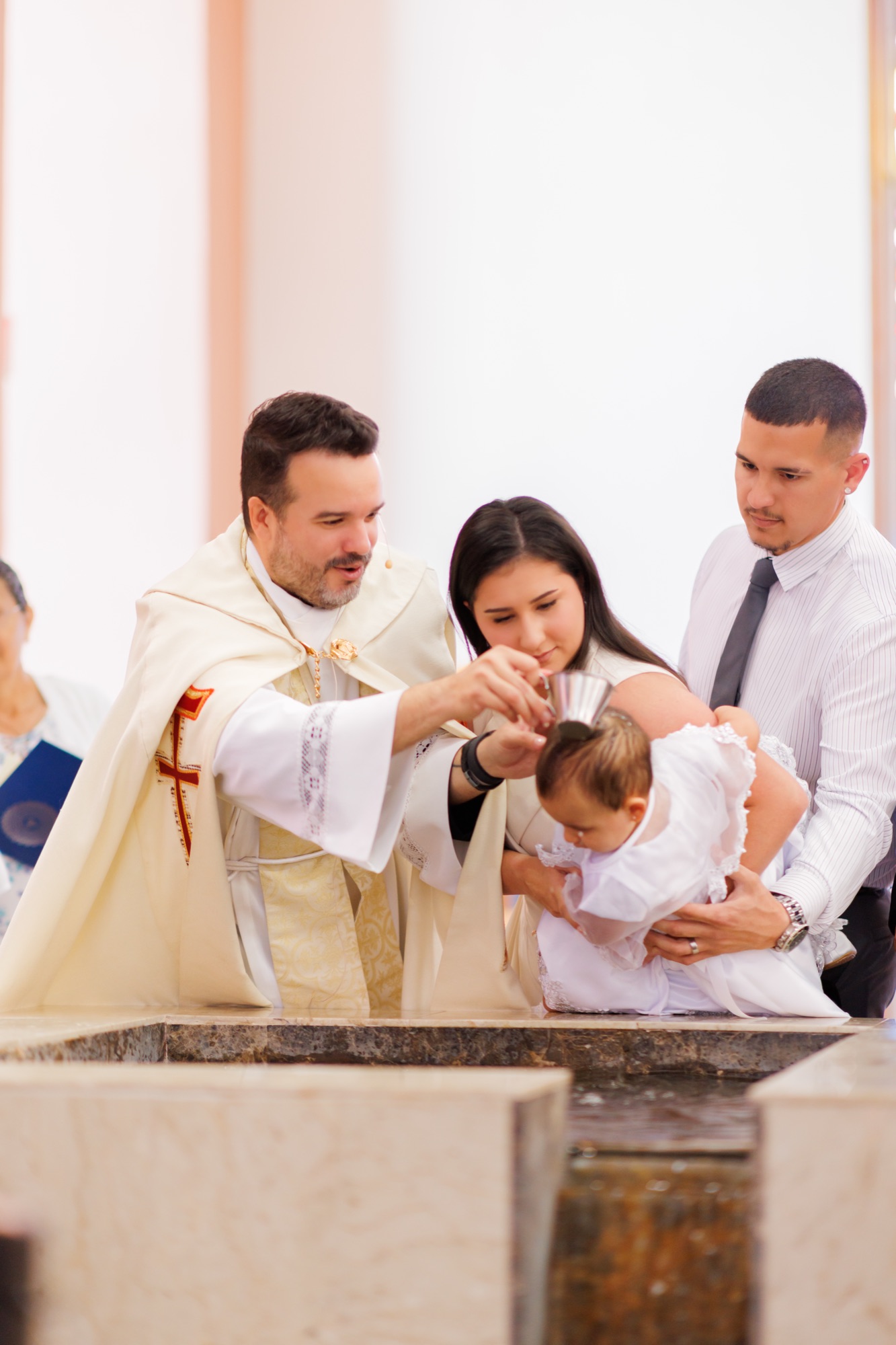 Priest pouring water over a baby held by the parents at a marble baptismal font