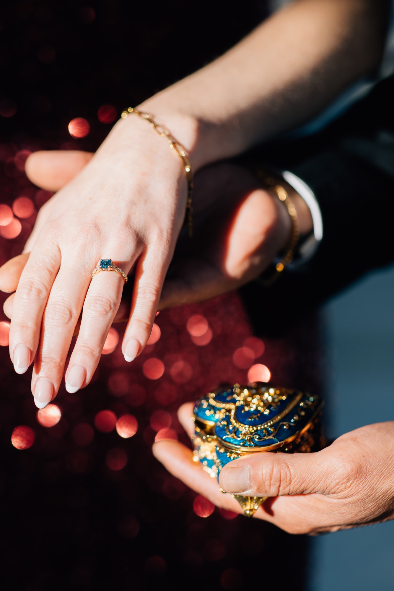 Hand with a sapphire engagement ring held above an ornate blue and gold ring box