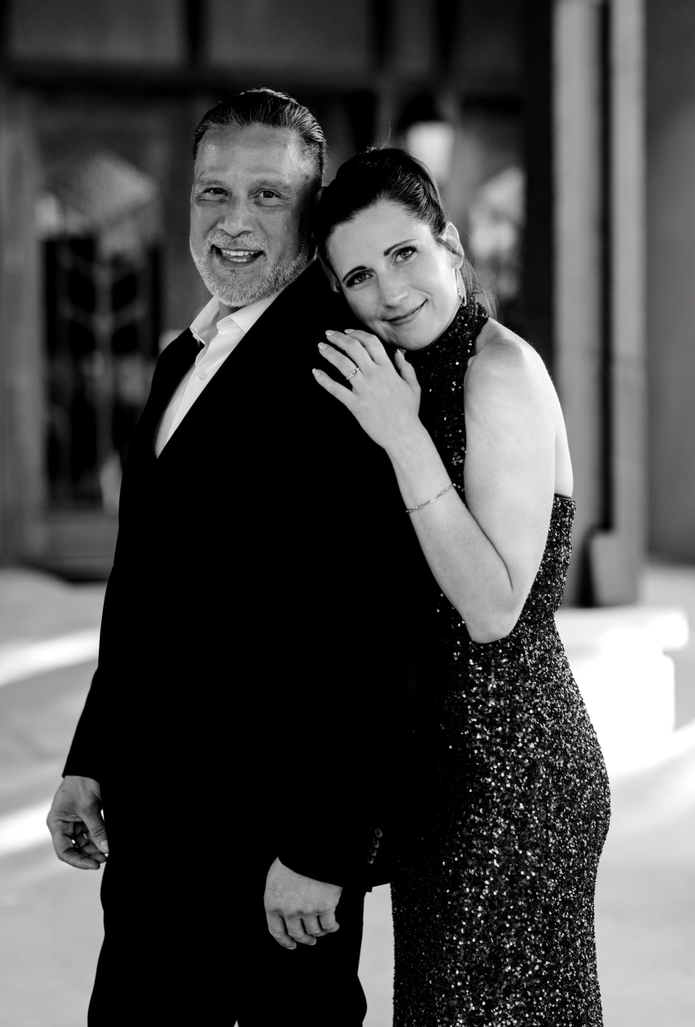 Black and white portrait of a couple in formal wear, her hands resting on his shoulder