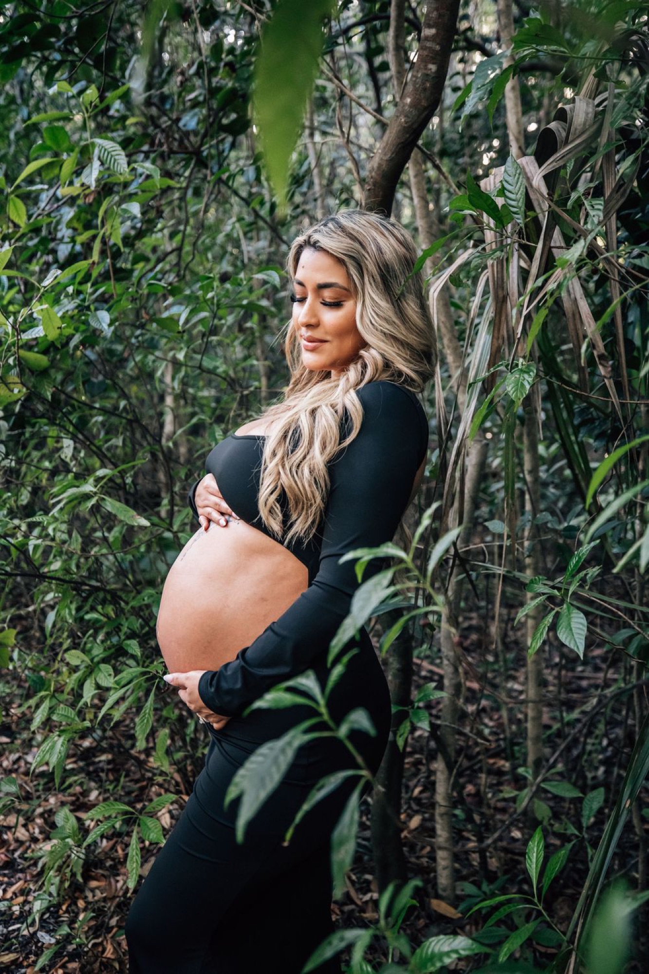 Expecting mother cradling her bump in a quiet wooded moment