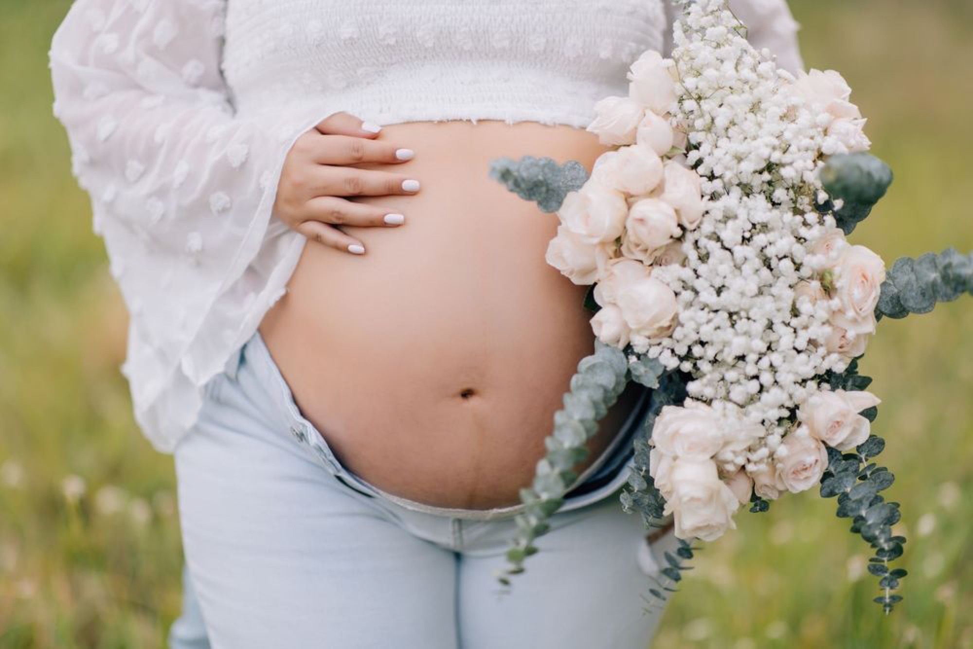 Close-up of a maternity bump cradled beside a blush rose bouquet