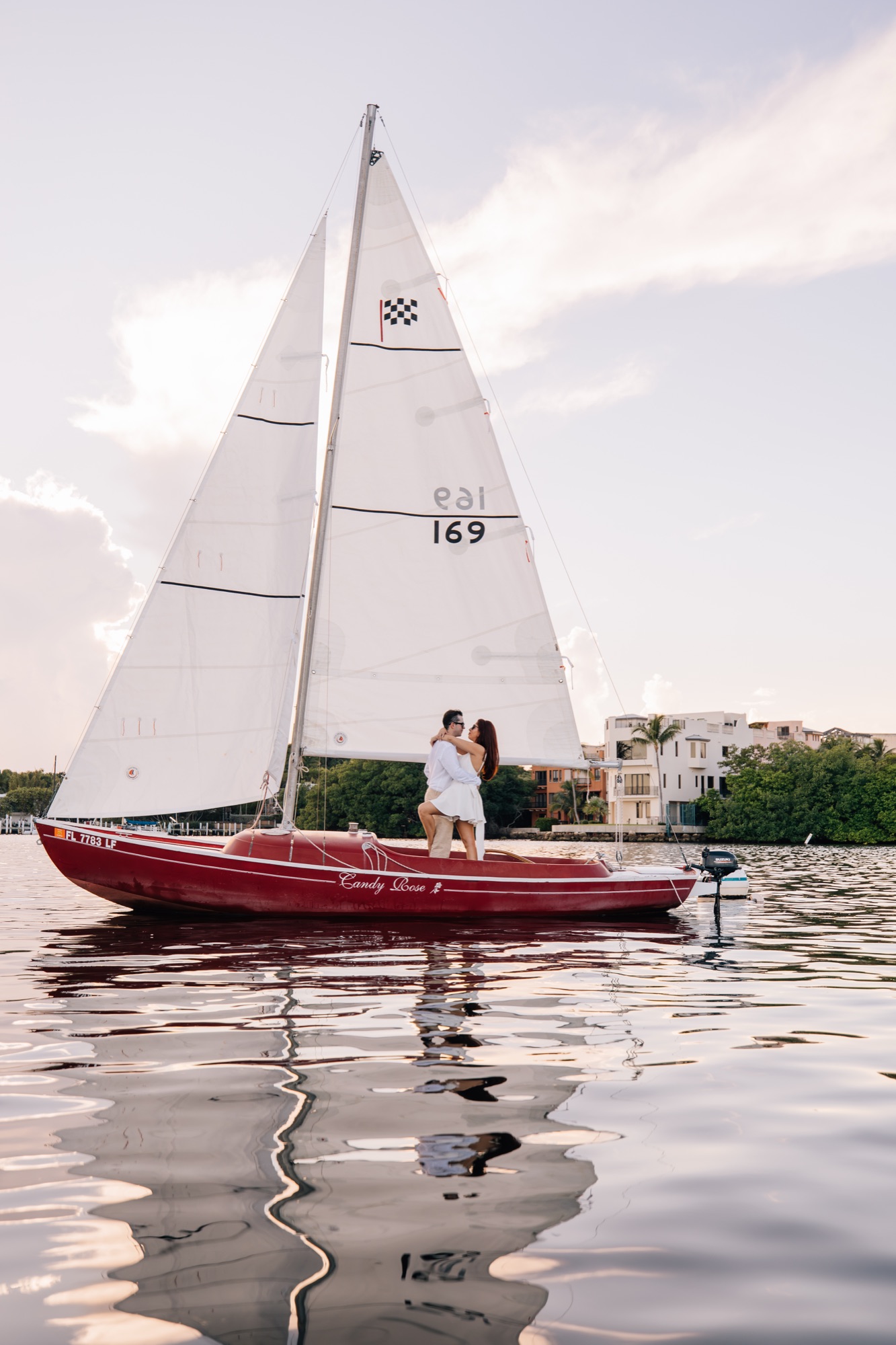 Couple embracing aboard a small red sailboat on calm Miami water at golden hour